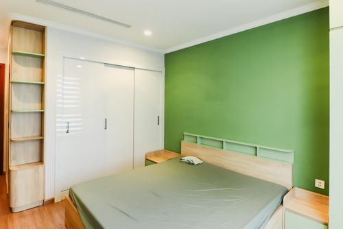 Free A minimalist bedroom featuring a green accent wall, wood furniture, and neutral bedding. Stock Photo