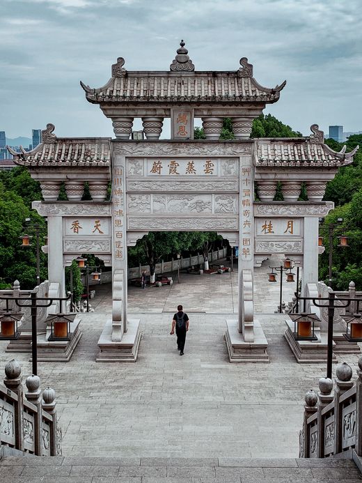 A carved stone ceremonial gate with a lone walker on the plaza below — photo by dh tang on Pexels