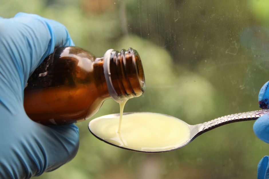 Close-up of liquid medicine being poured into a spoon, captured with gloves for medical use.