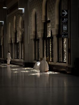 Quiet interior scene with people in white robes, showcasing intricate architectural details and subtle lighting.