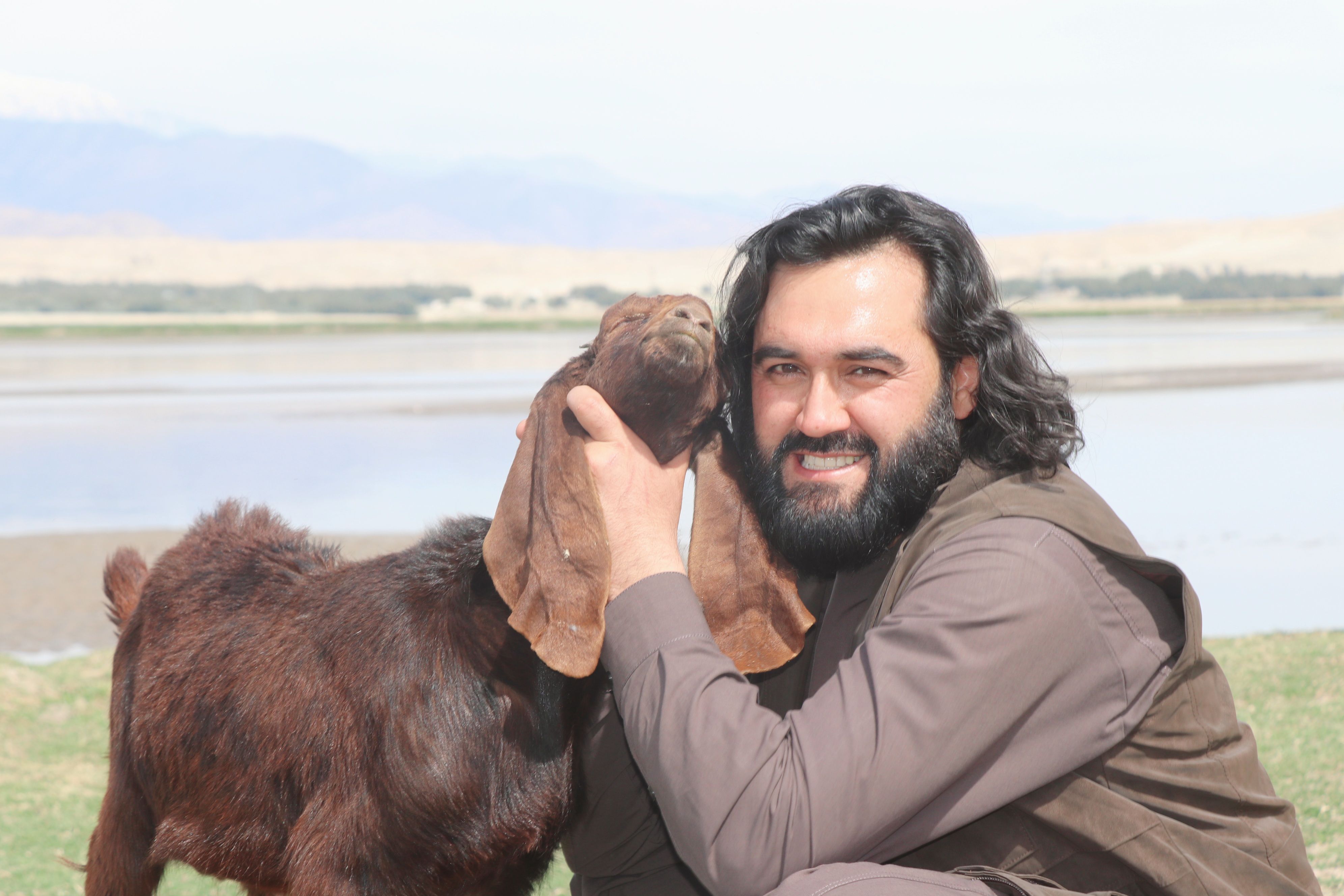 Man Cuddling Goat by the Lakeside Outdoors