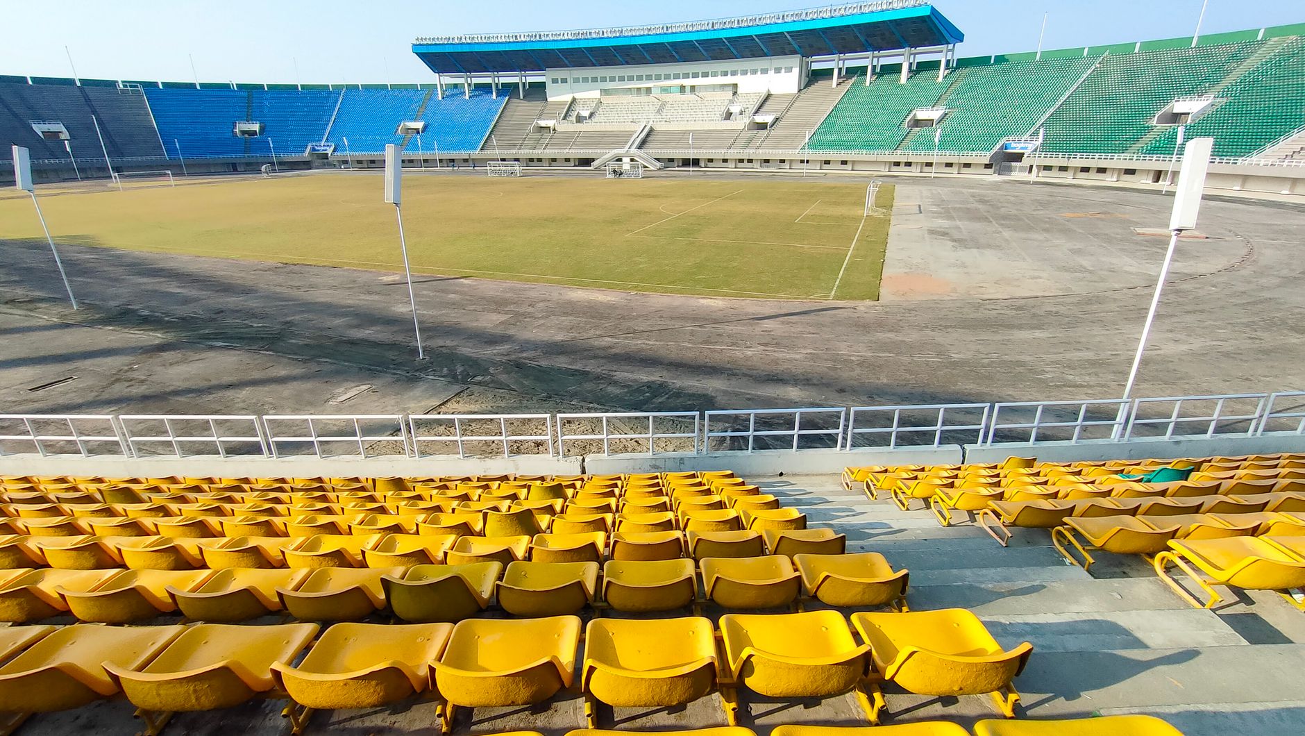 A wide shot of an empty stadium with colorful seating under bright daylight.