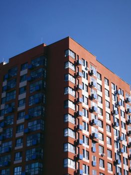A modern high-rise apartment building captured from below against a clear blue sky.