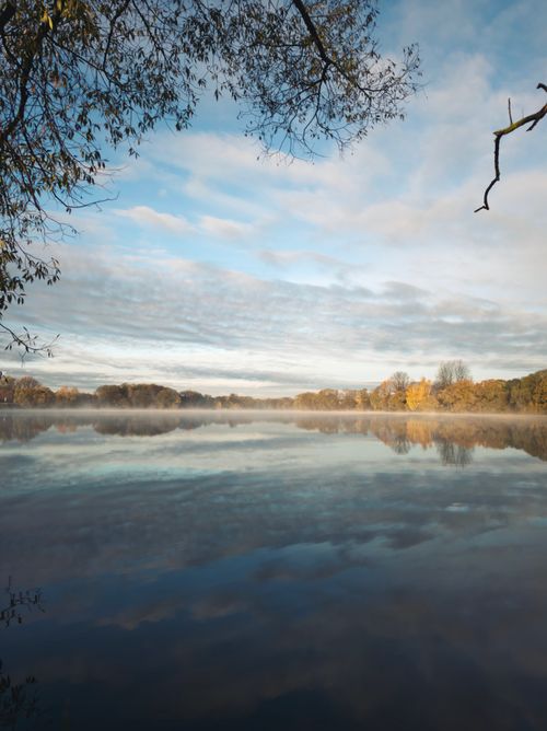 Free Peaceful lake scene at sunrise with autumn foliage reflecting in calm waters. Stock Photo