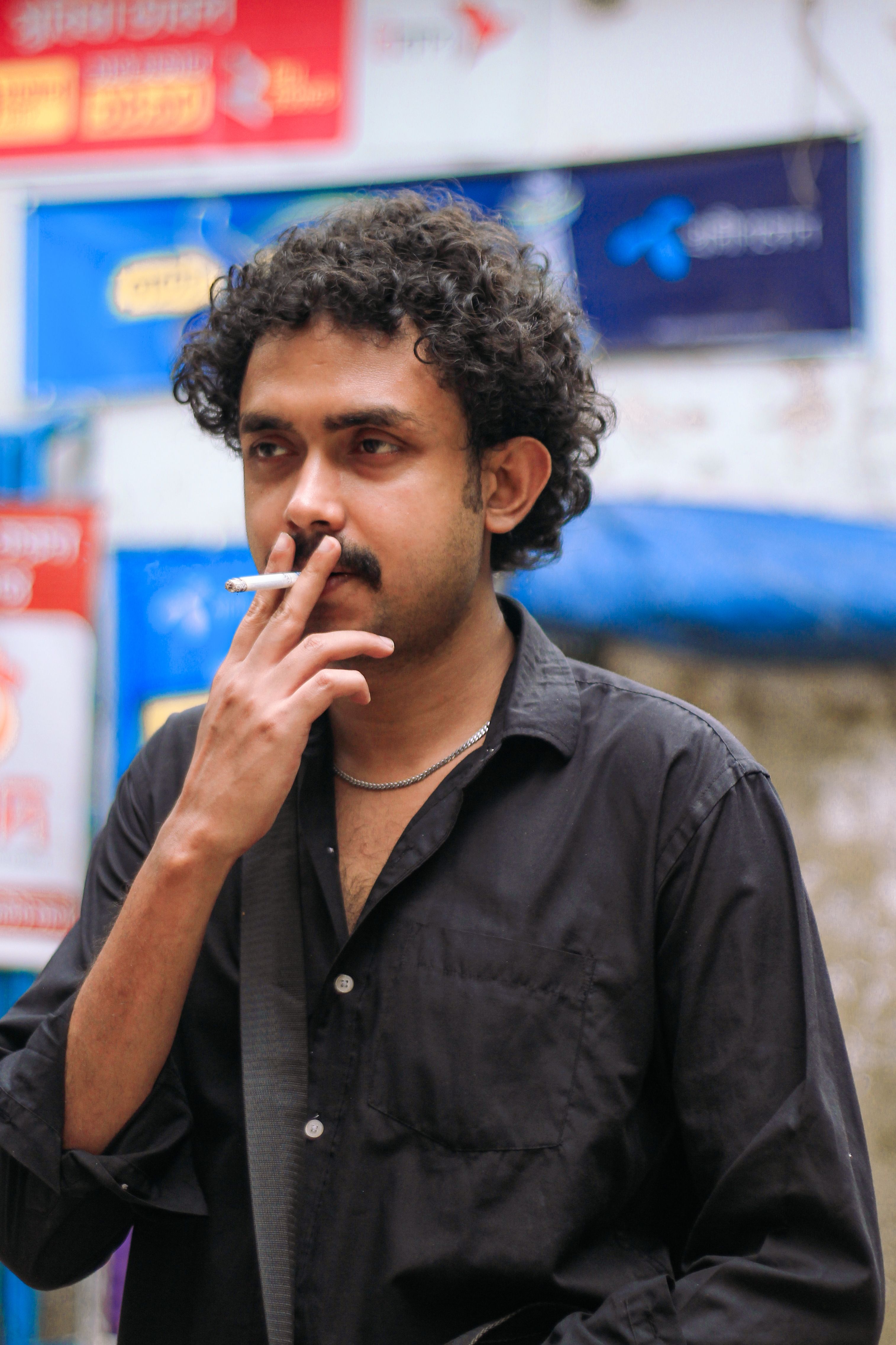 Portrait of a man smoking on a bustling street in Dhaka, showcasing urban life.