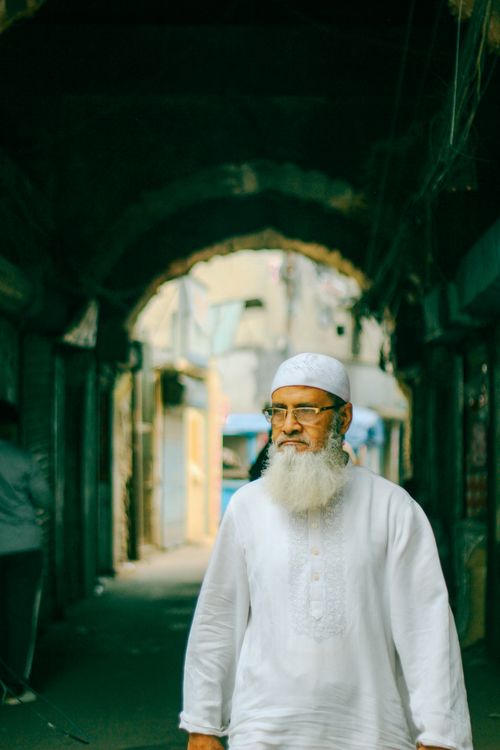 Free Senior man in traditional attire walks through a narrow alley in Old Dhaka, Bangladesh, showcasing cultural heritage. Stock Photo