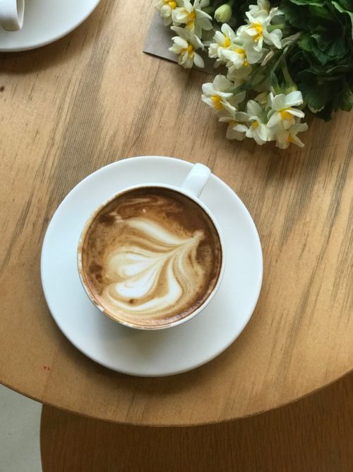 Free Overhead view of a cappuccino with latte art beside fresh flowers on a wooden table. Stock Photo