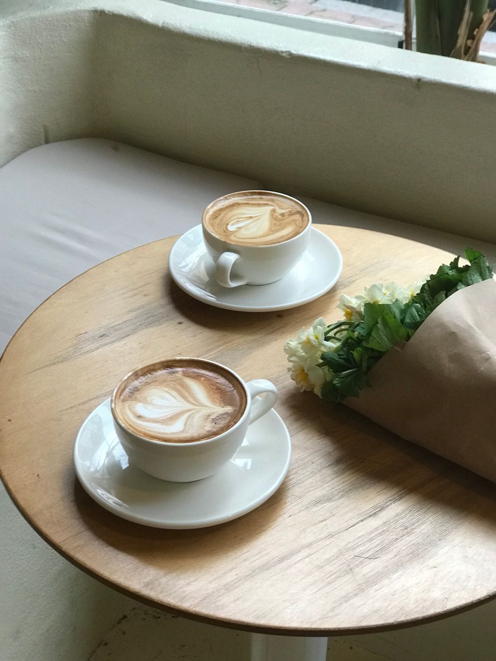 Two cappuccinos with heart latte art and flowers on a wooden table, creating a cozy café atmosphere.