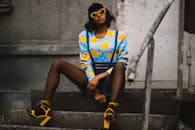 一位时尚的黑人妇女，身穿五颜六色的衣服，戴着大胆的眼镜，站在城市楼梯上