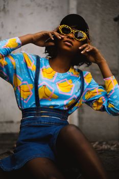 Stylish black woman posing in colorful streetwear and sunglasses, embodying urban fashion and confidence.