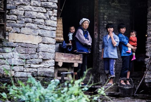 Free Traditional Chinese family stands outside their rustic stone home, showcasing rural lifestyle. Stock Photo