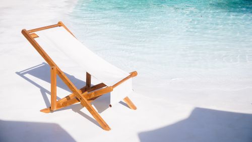 Free A wooden deck chair placed near a clear, refreshing pool under the bright sun. Stock Photo