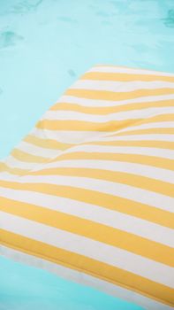 Yellow and white striped pool float on serene clear blue water, capturing a summer vibe.