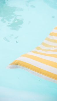 A vibrant yellow and white striped float gently resting in clear pool water. Perfect summer vibes.