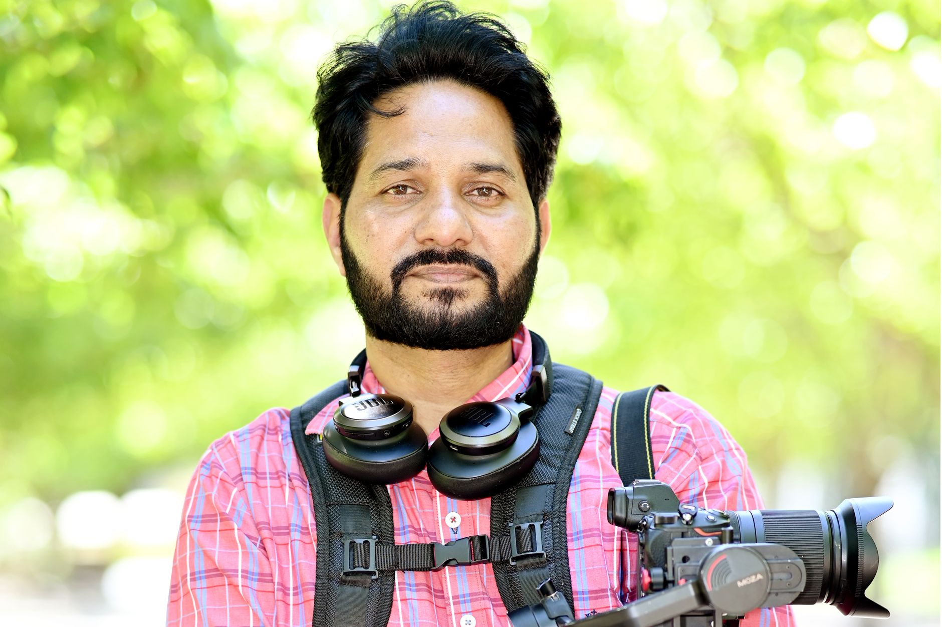 Confident videographer with headphones and camera in a sunny outdoor setting.