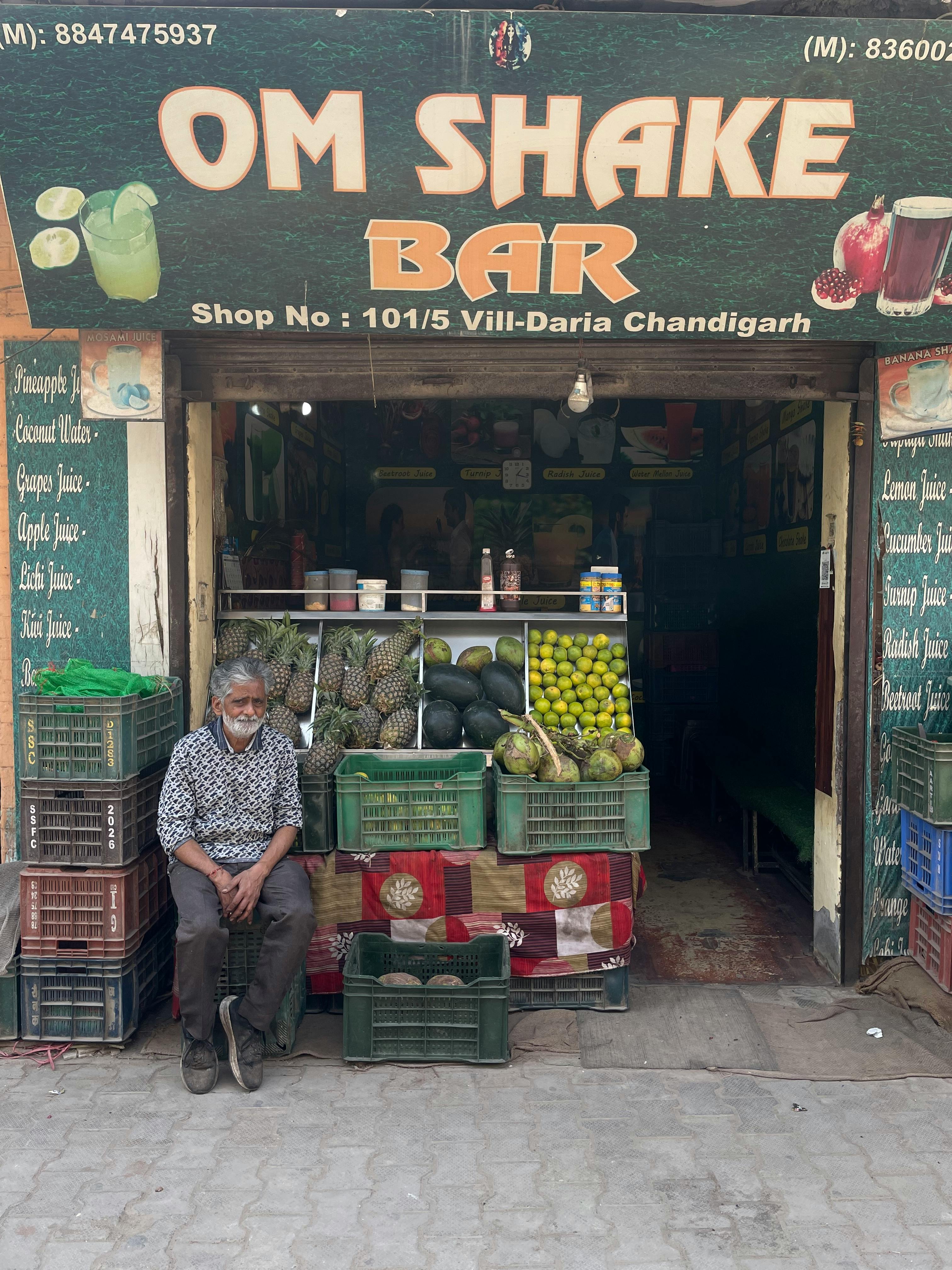 Outdoor view of a fruit juice bar in Chandigarh, India with fresh fruits displayed and a person seated.