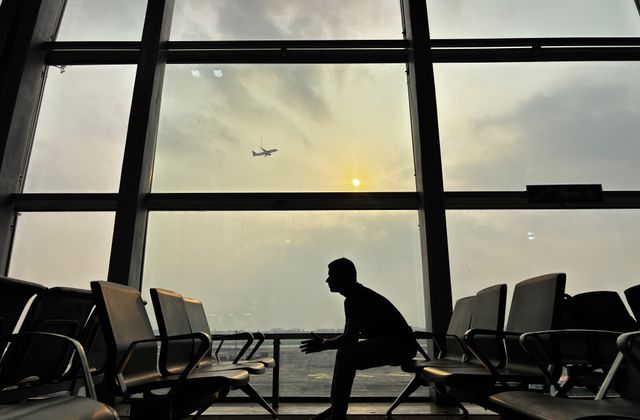 Silhouette of a man sitting at Kolkata Airport with a plane in the sky during sunset. — arriving in Kolkata