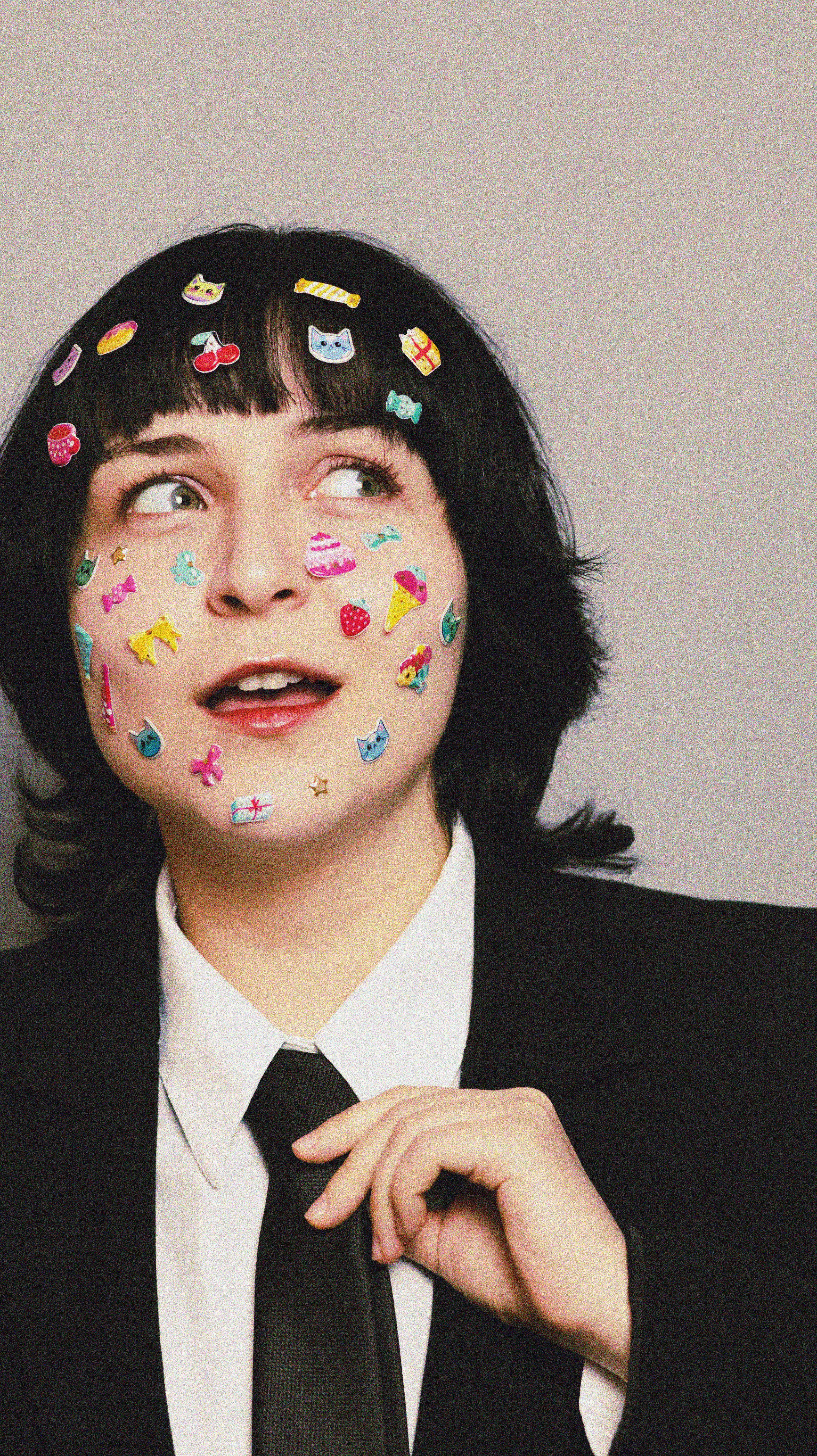 Fun portrait of a person with colorful stickers on their face in a suit, showcasing creativity.
