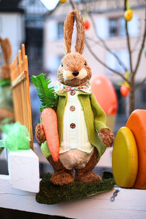 Free Adorable Easter bunny decoration with carrot, colorful eggs, and festive setup. Stock Photo