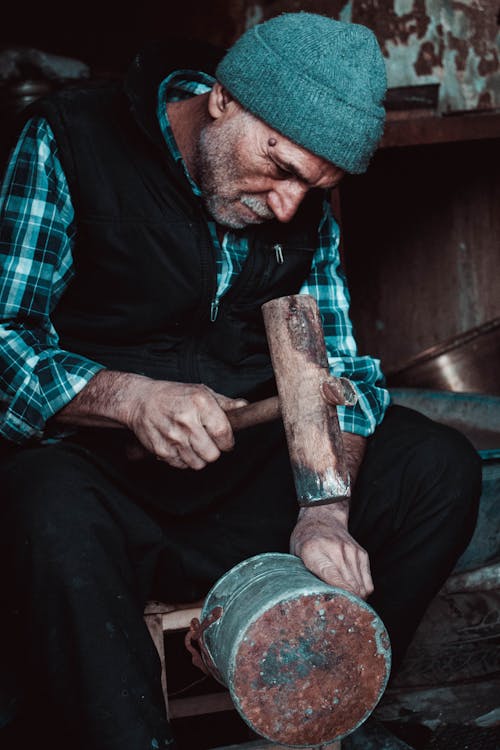 An Elderly Man Fixing A Can With A Hammer