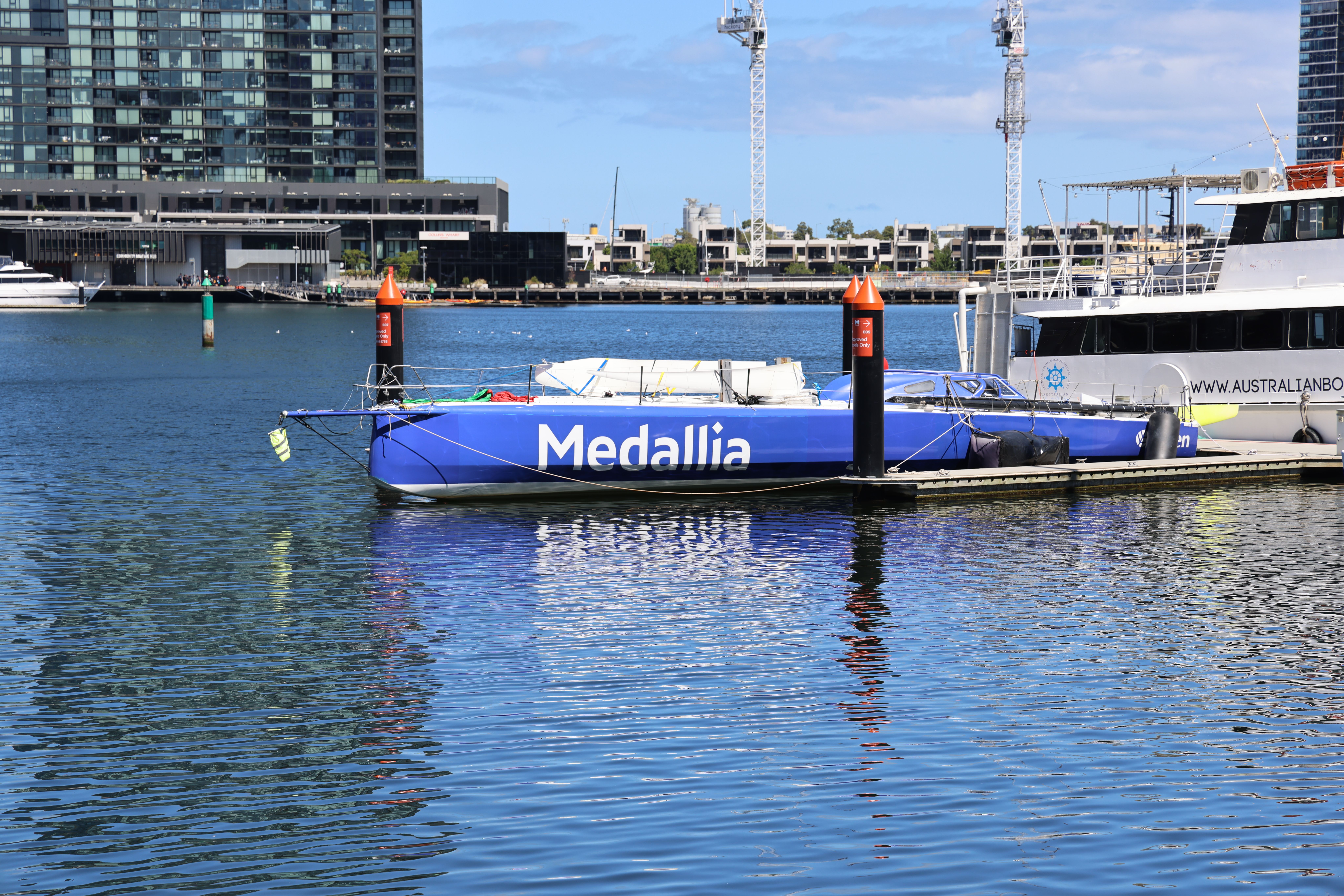Blue sailboat 'Medallia' docked at a modern marina on a sunny day.