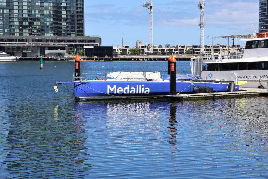 Blue sailboat 'Medallia' docked at a modern marina on a sunny day.