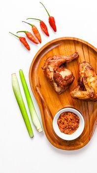 Tasty grilled chicken served with chili peppers and sauce on a wooden tray.