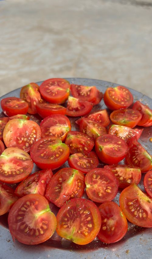 Free Bright red cherry tomatoes halved on a silver plate, sunlit outdoors. Stock Photo