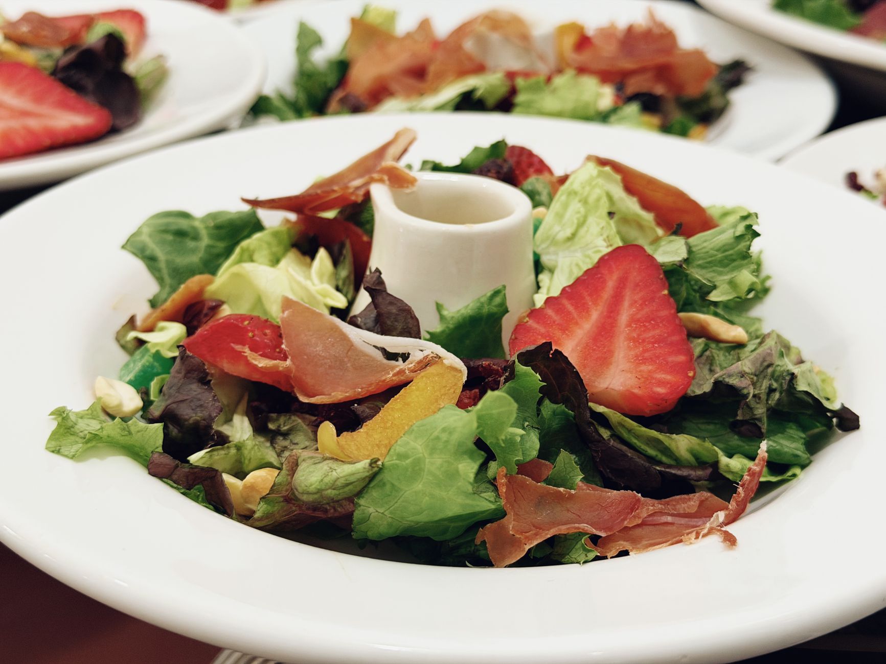 Delicious salad featuring strawberries, prosciutto, and mixed greens on a white plate.