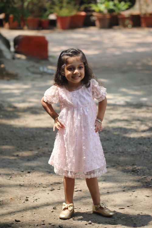 Free Cheerful young girl in a pink dress enjoying a sunny day outside. Stock Photo