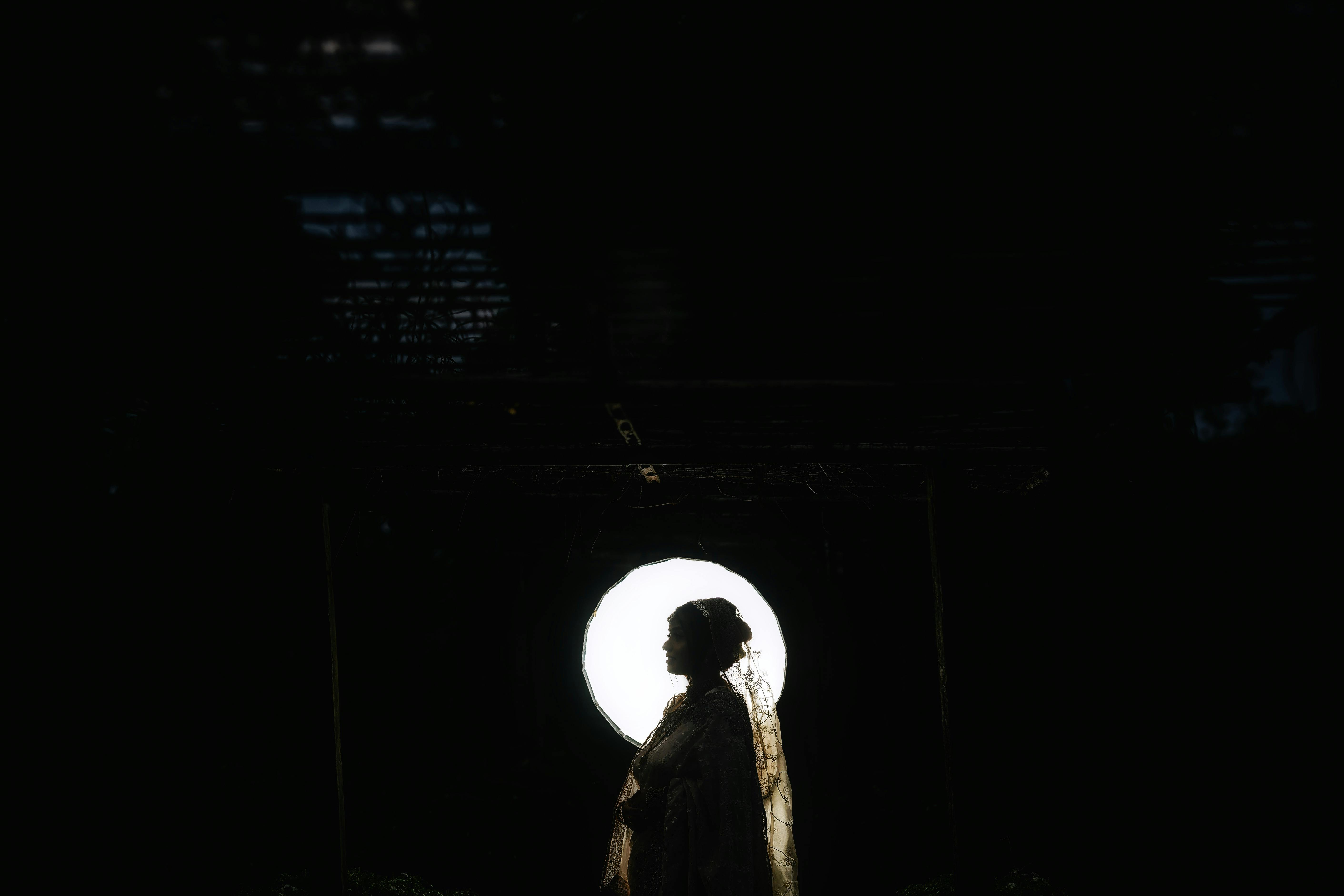 Dramatic silhouette of a person against a bright circular backdrop, emphasizing mystery and contrast.