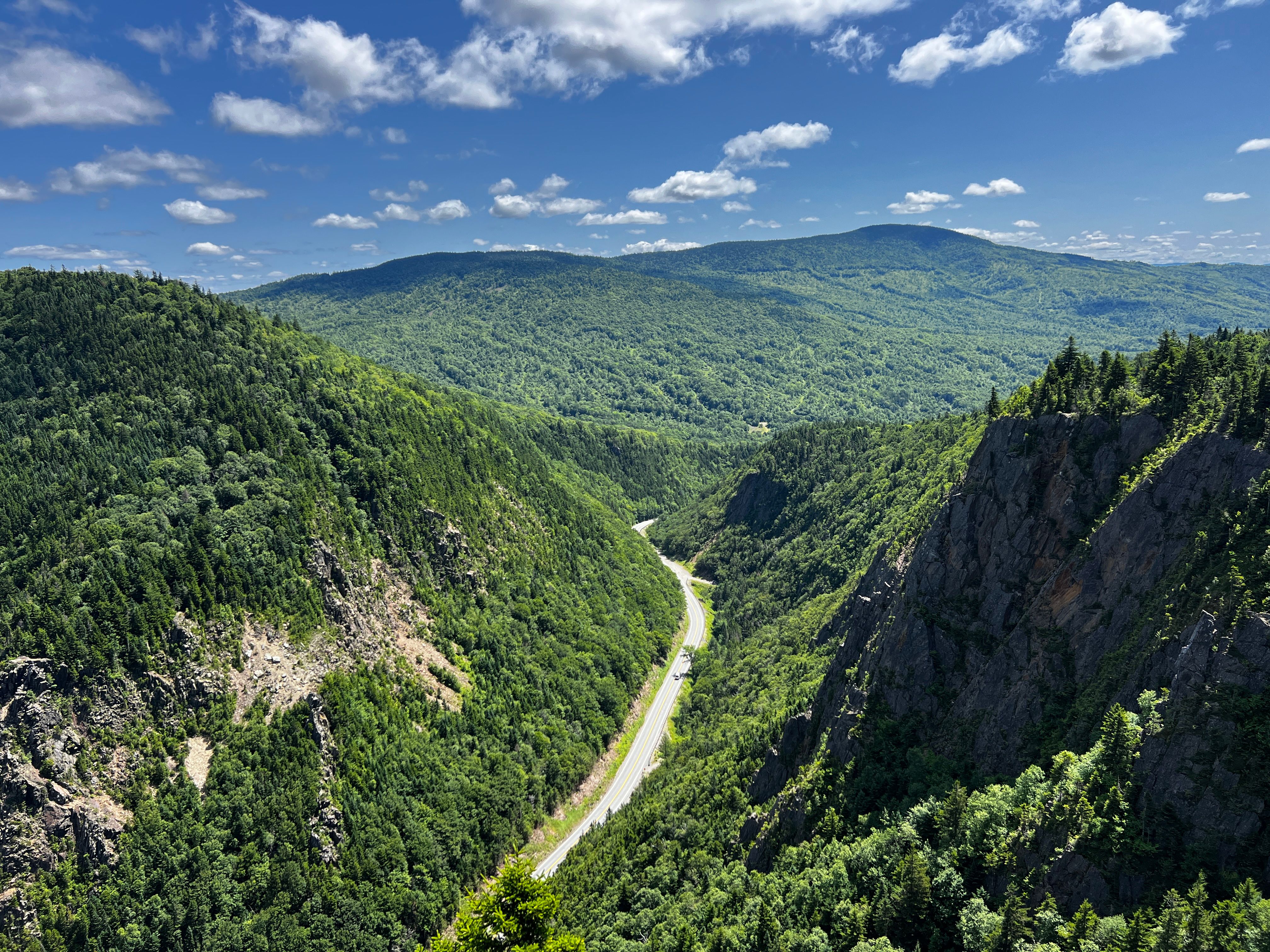 Breathtaking aerial view of lush green forests in the Notch Region, a serene highway winding through the mountains.