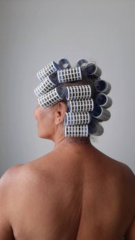 A senior woman with hair curlers set, viewed from behind indoors with natural light.