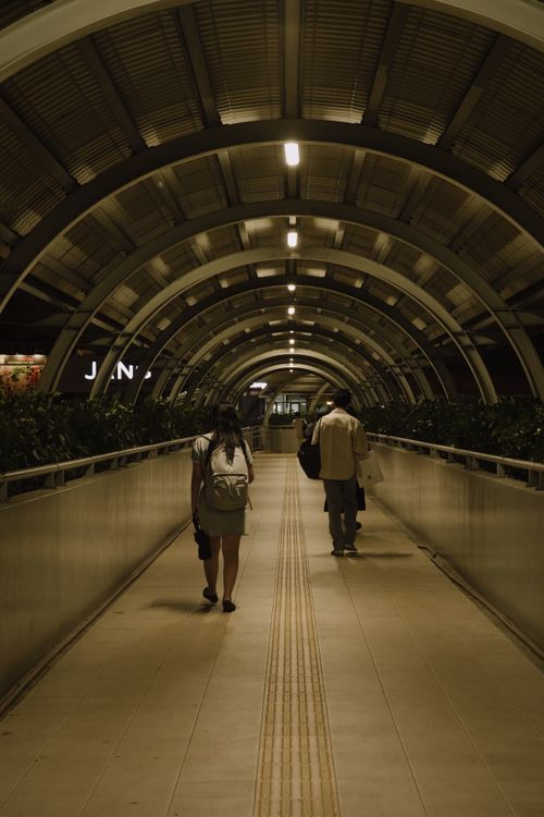 Free Two individuals walk in a well-lit modern tunnel with an arched design. Stock Photo