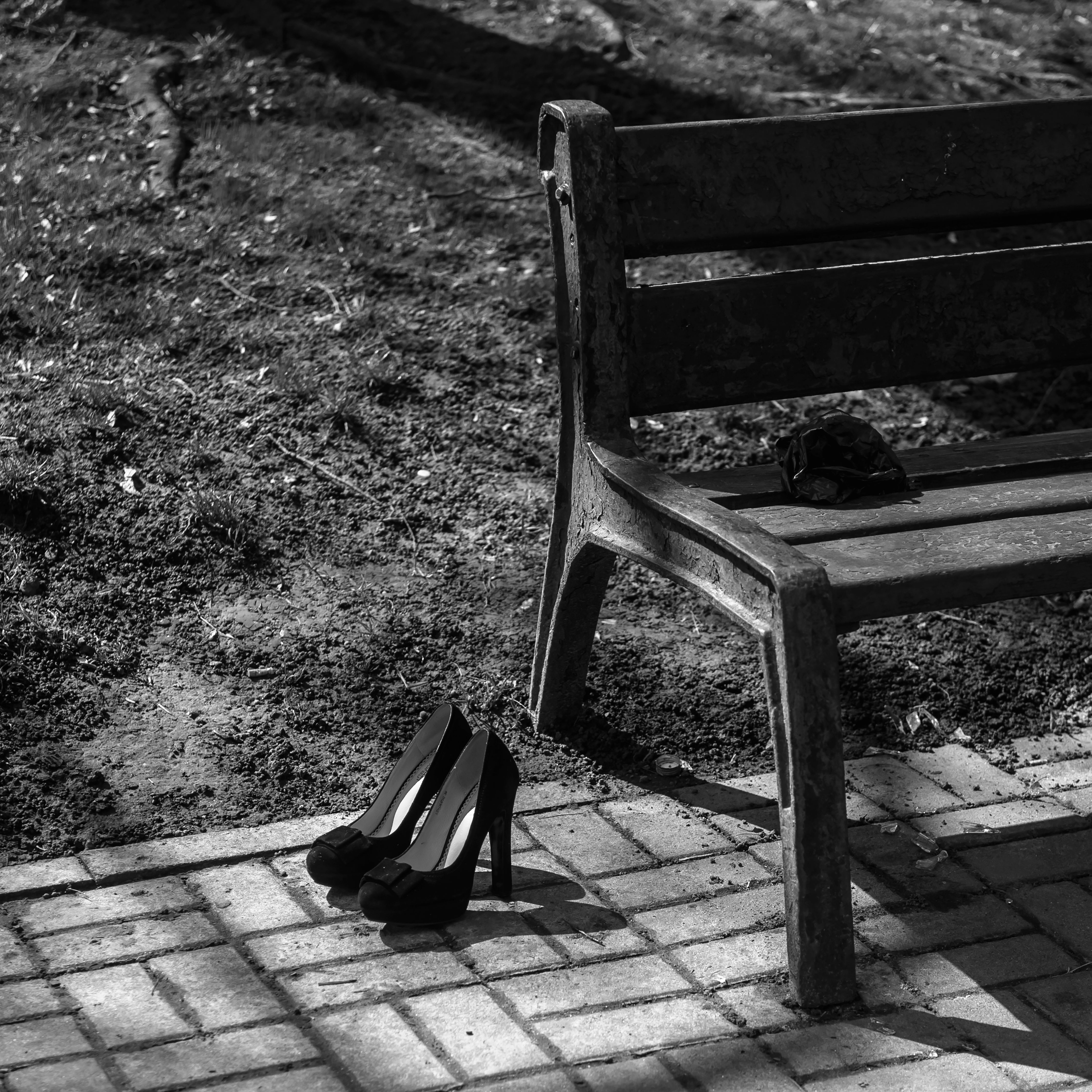 Black and white photo of high heels next to a park bench on a sunny day.