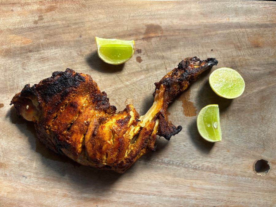 Tandoori chicken leg served with fresh lime on a rustic wooden board