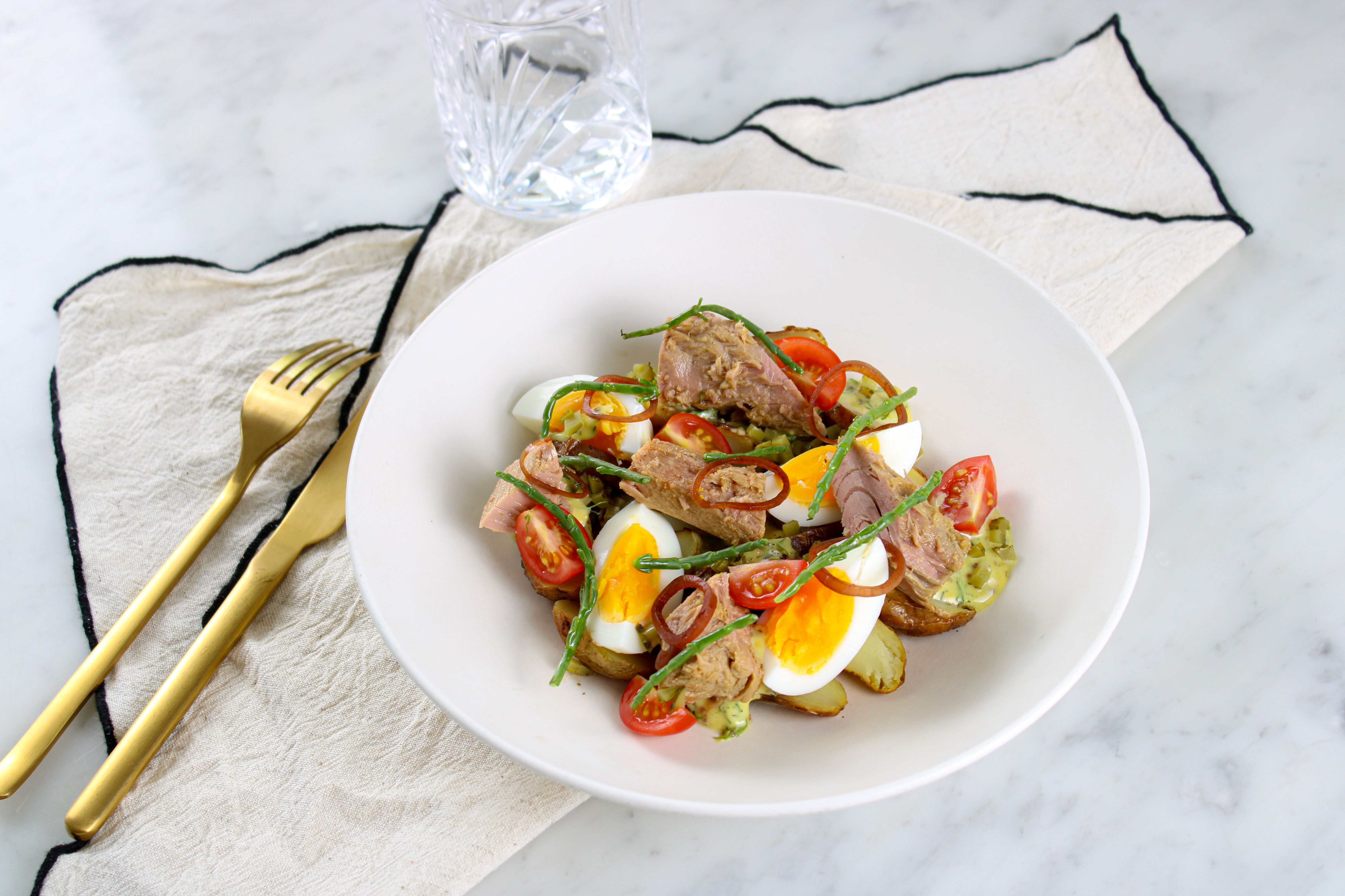 A fresh tuna salad featuring boiled eggs, cherry tomatoes, and greens, elegantly plated.