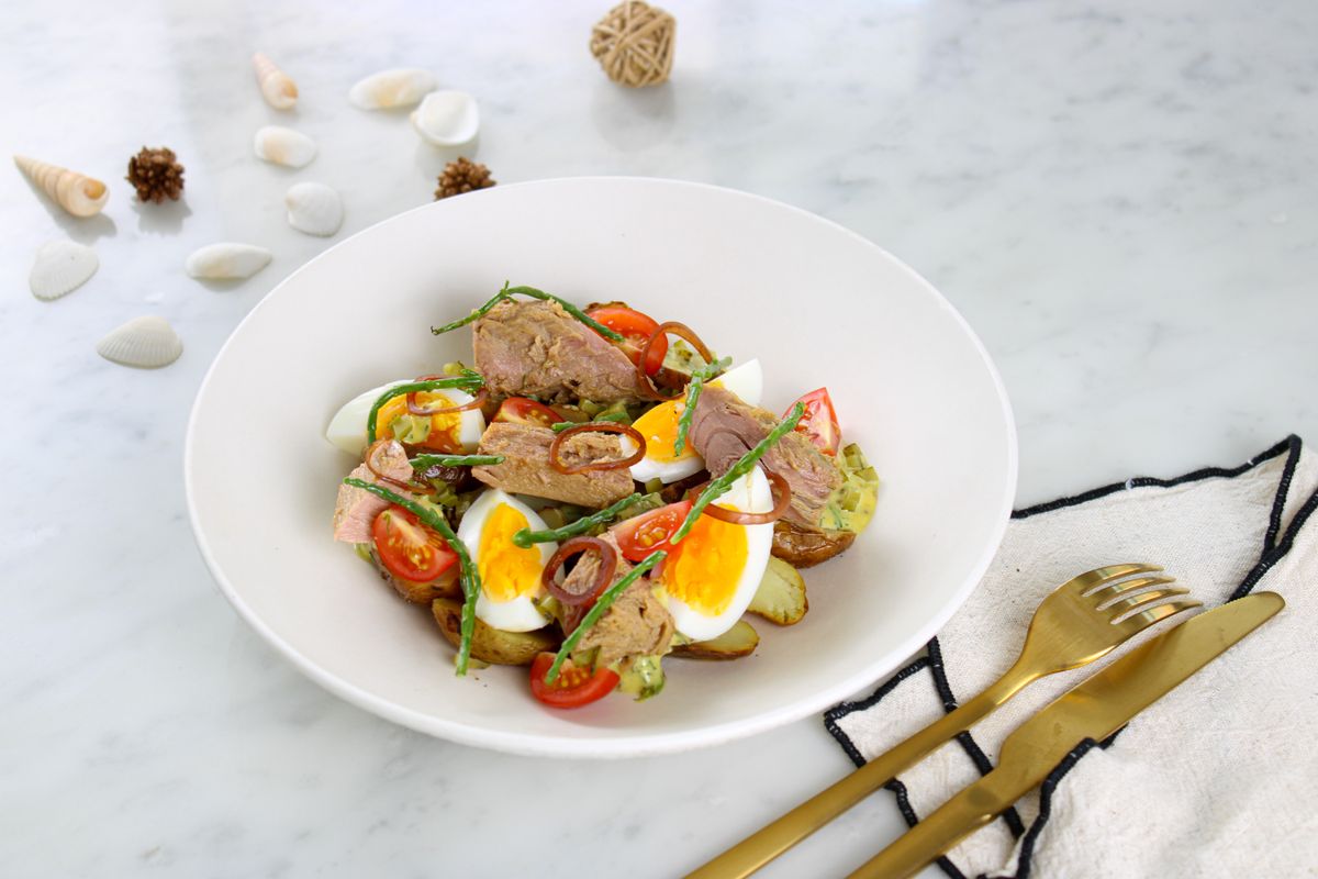Tuna chunks, halved eggs, cherry tomatoes, baby potatoes and green beans in a white bowl