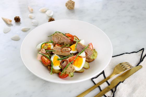 Tuna chunks, halved eggs, cherry tomatoes, baby potatoes and green beans in a white bowl