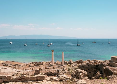 Scenic view of ancient ruins in Sardinia, Italy, with yachts on the Mediterranean Sea in summer.