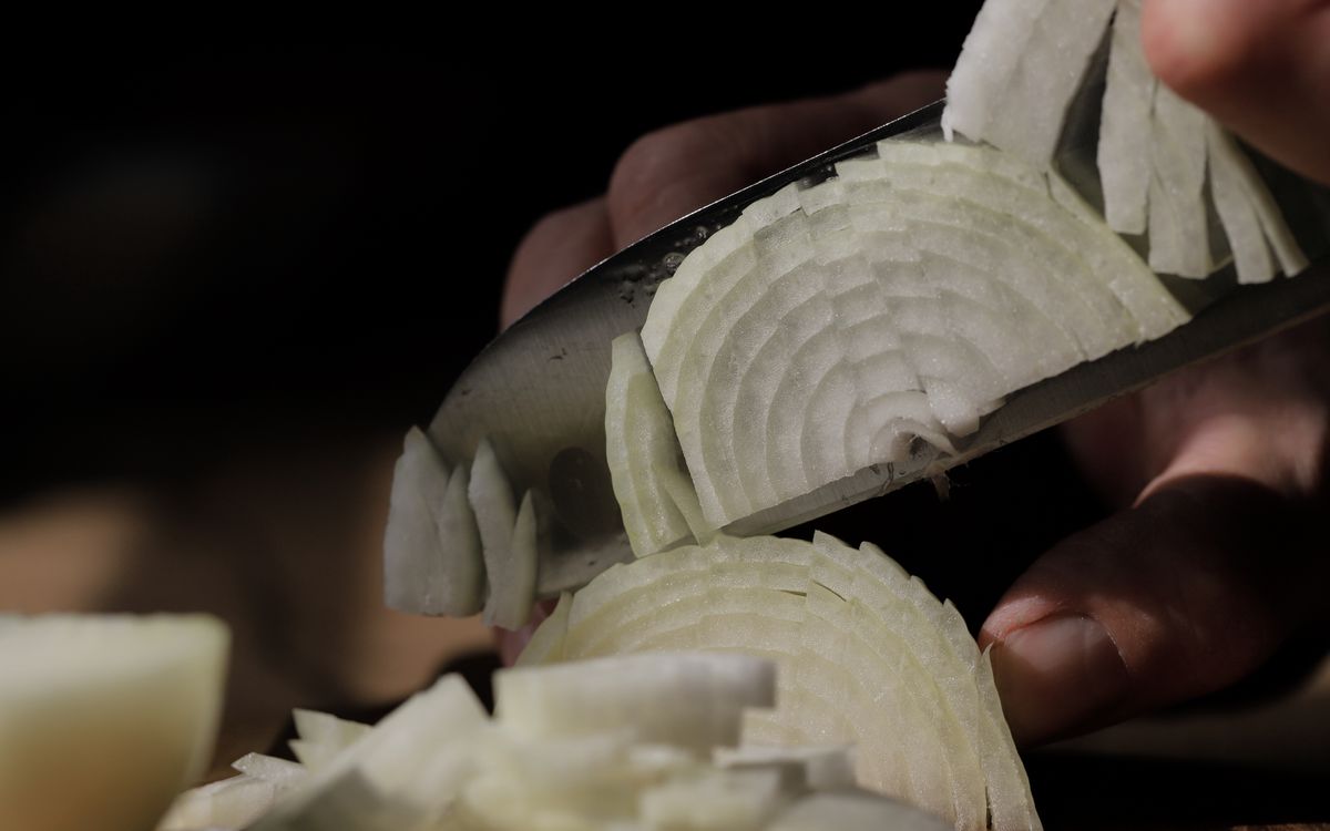 Detailed shot of slicing white onions with a sharp knife, perfect for cooking themes.