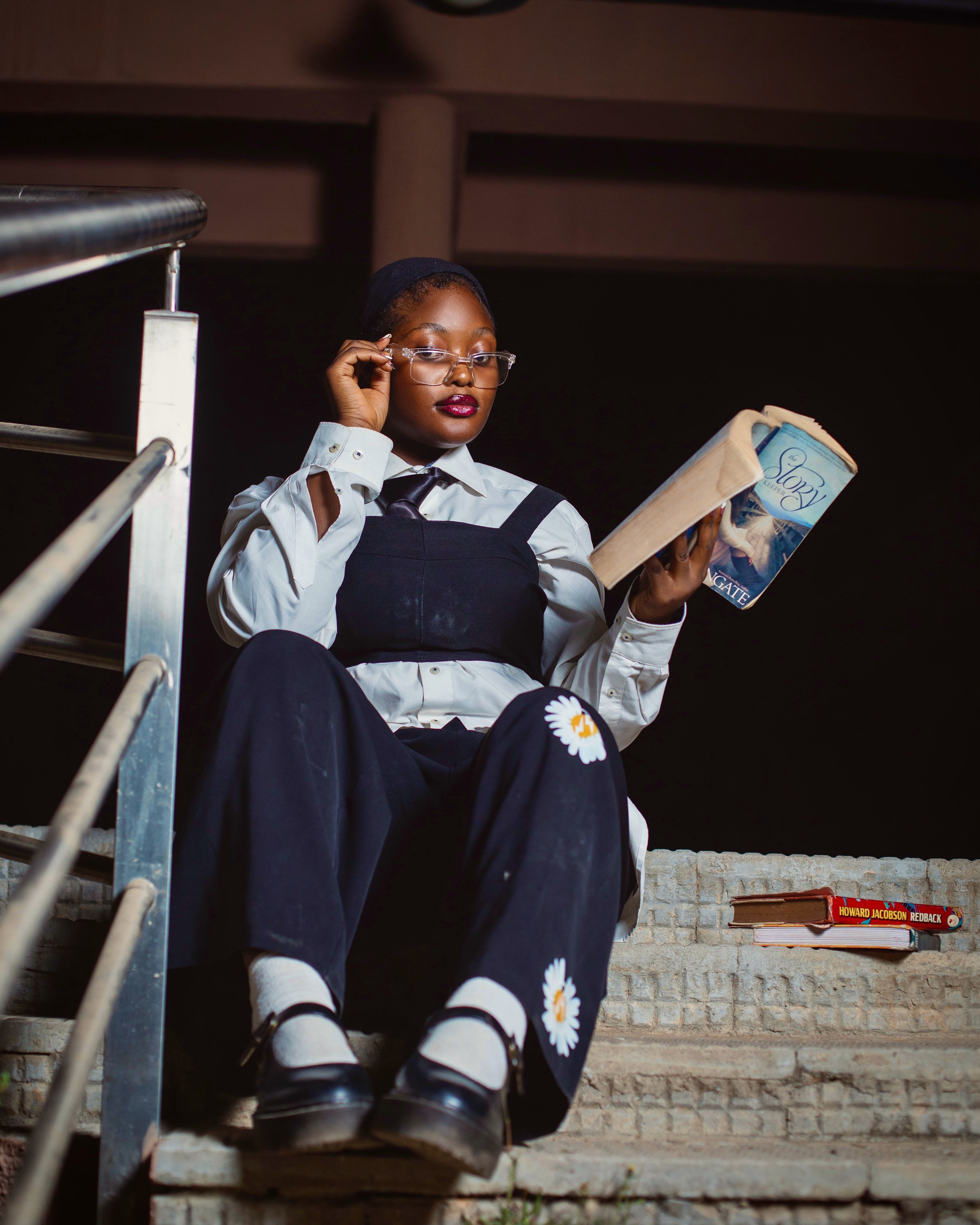 Woman in glasses reads on stairs at night, exuding focus and contemplation.
