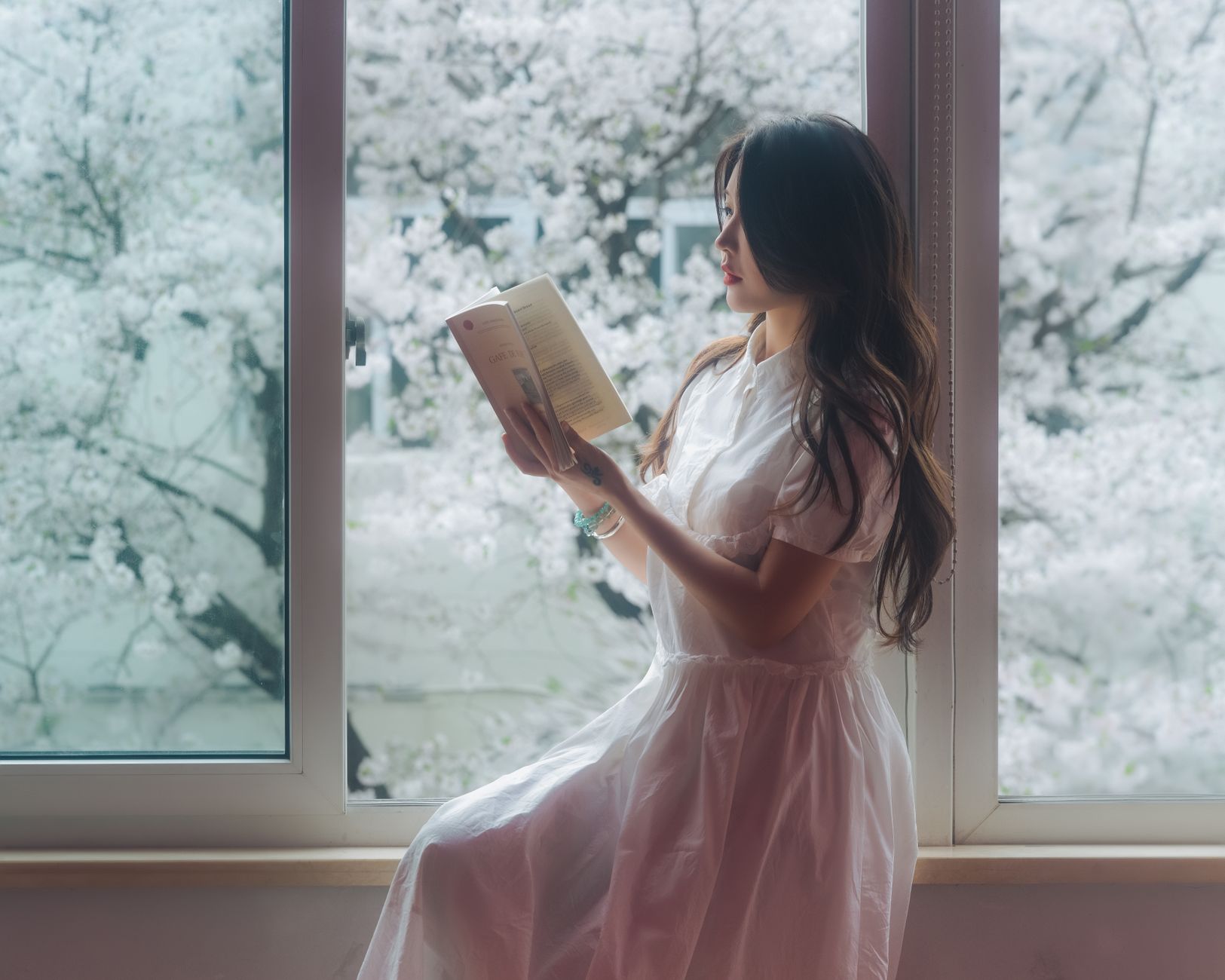 A serene image of a woman reading by a window with cherry blossoms outside, capturing a peaceful spring moment.