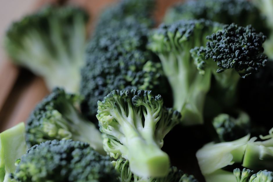 A whole head of broccoli next to a cutting board of separated florets and sliced stems, showing the tight dark green buds and pale interior stalk.