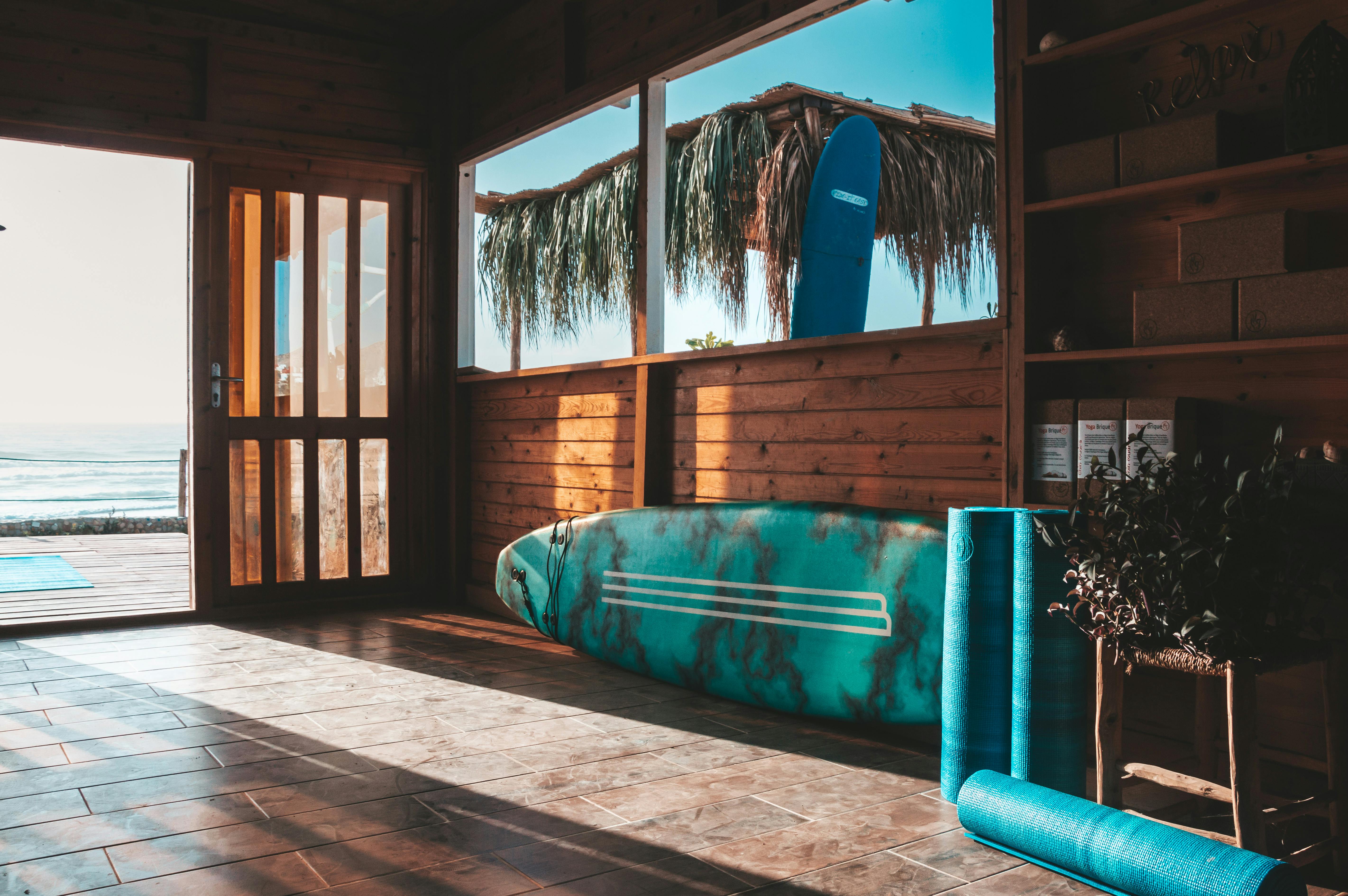 Wooden surf shack interior with surfboard and yoga mat overlooking the ocean at sunrise in Taghazout, Morocco.