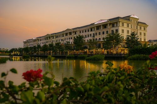 Free Elegant building by a lake at sunset, surrounded by trees and flowers, offering a serene urban landscape. Stock Photo