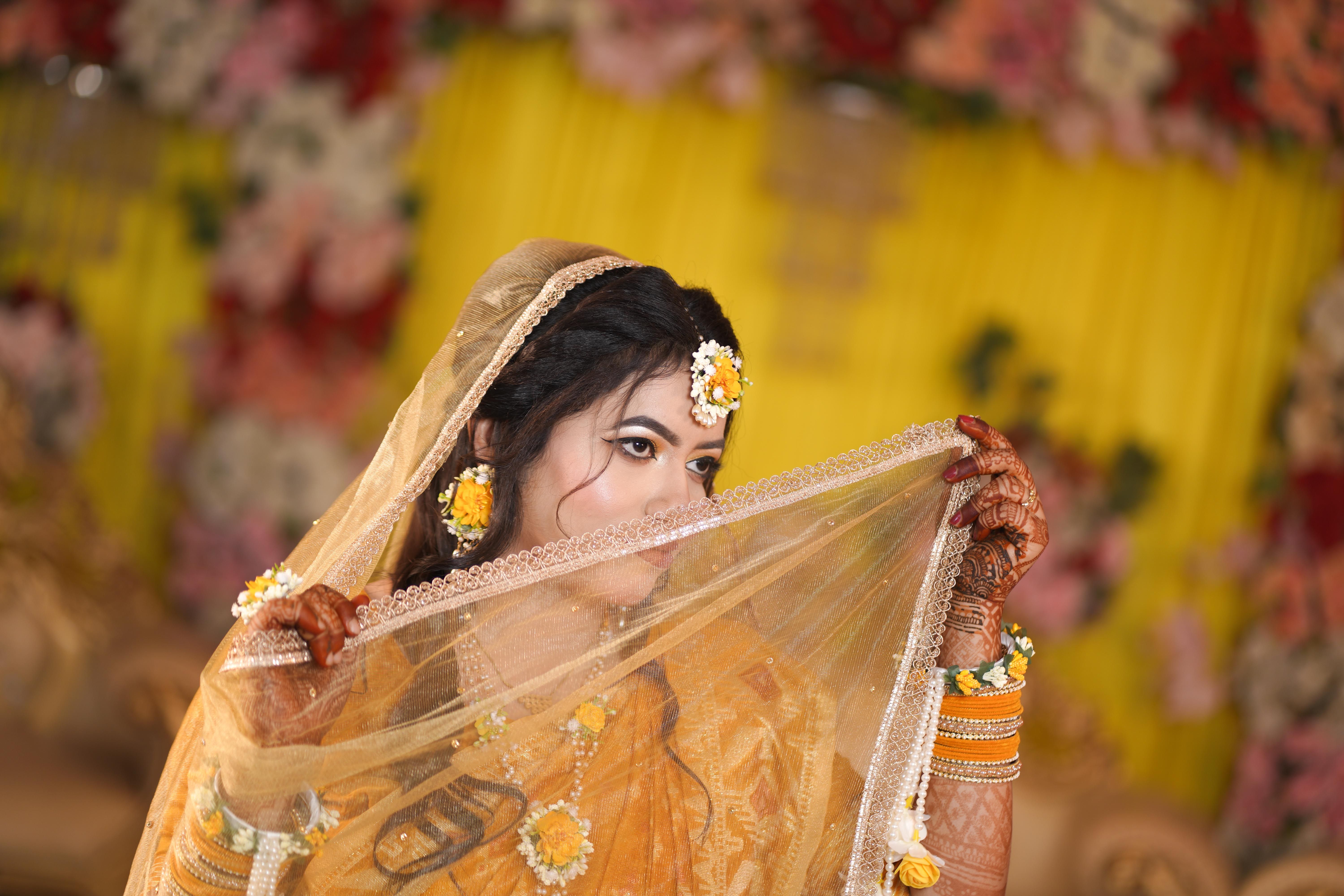 Stunning bride in traditional attire holding a lace veil with floral decorations in the background.