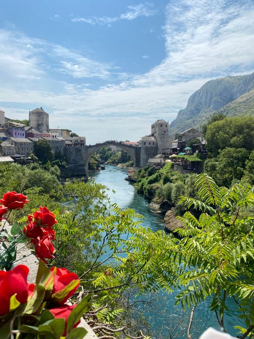 Free Captivating view of the Old Bridge and river in Mostar, Bosnia with vibrant flowers in the foreground. Stock Photo