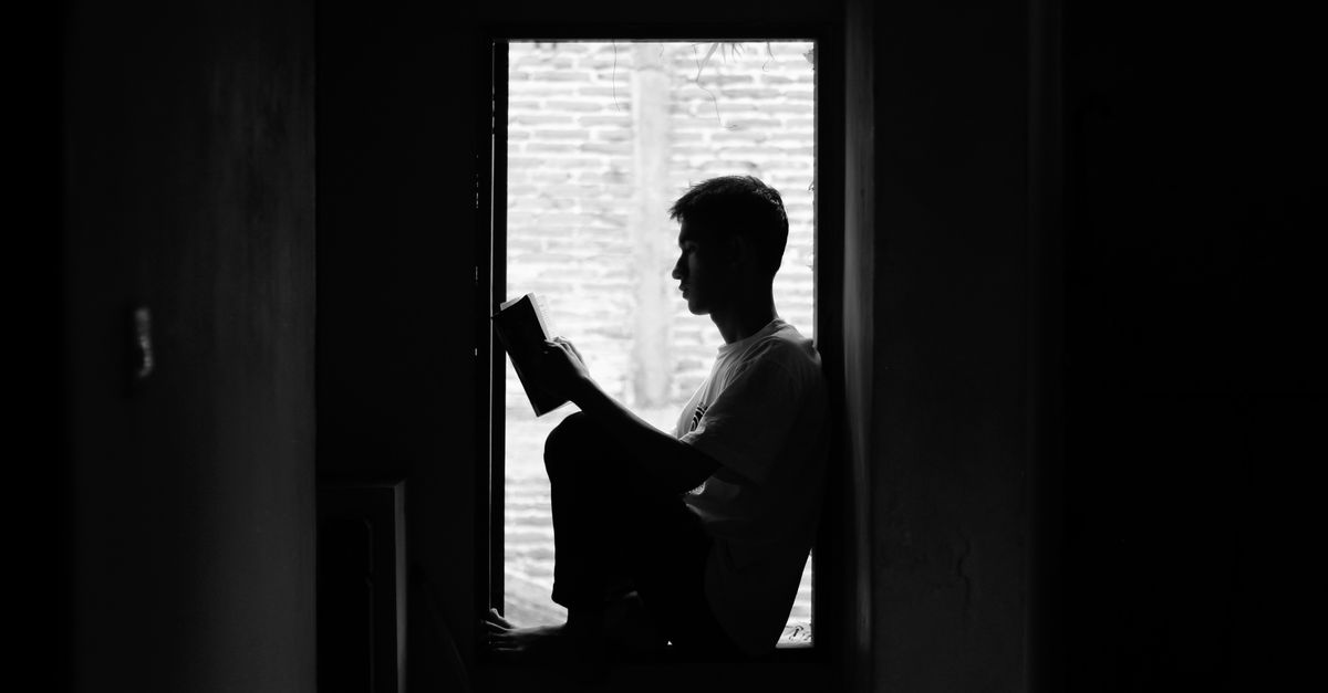 A black and white image of a person reading by a window, capturing a sense of quiet contemplation.