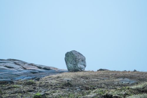 Free A large rock stands alone on a grassy hill with clear blue sky in the background. Stock Photo